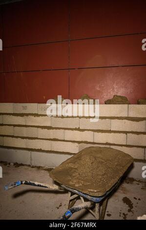 Building a wall in progress. Wheelbarrow with prepared masonry mortar. Transport infrastructure construction site concept. Stock Photo