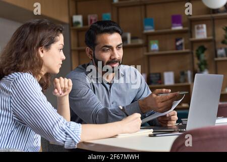Indian teacher or mentor helping latin student, teaching intern using laptop. Stock Photo