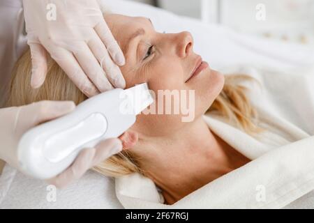 Senior woman in professional beauty spa salon during ultrasonic facial cleansing procedure Stock Photo