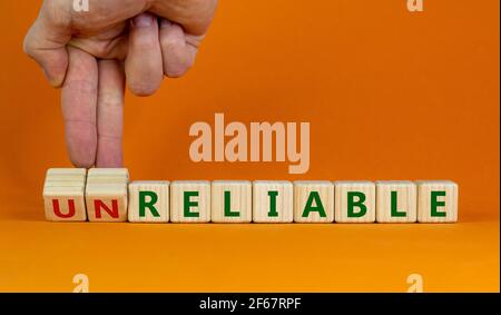 Unreliable or reliable symbol. Businessman turns wooden cubes and changes the word unreliable to reliable. Beautiful orange background, copy space. Bu Stock Photo