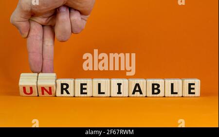 Unreliable or reliable symbol. Businessman turns wooden cubes and changes the word unreliable to reliable. Beautiful orange background, copy space. Bu Stock Photo