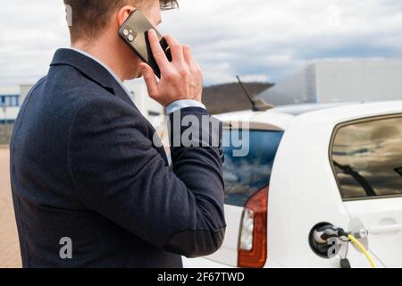 Business man standing near the charging electro and talking on the smartphone  Stock Photo