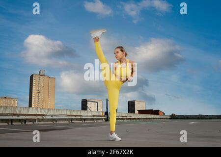 Attractive sporty woman wearing yellow activewear practicing high kick exercise outside in an urban setting. Stock Photo