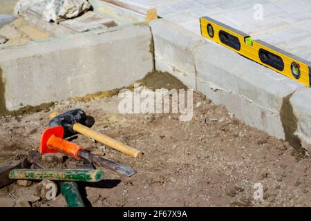 Defocus Paving garden. Yellow spirit level, hammer, mallet, chisel lie on the ground. Set of tools for laying paving stones. Cement curbs. Garden Bric Stock Photo