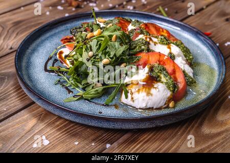 Sliced tomatoes and mozzarella lie on a plate seasoned with herbs, garnished with chili pepper and cinnamon.