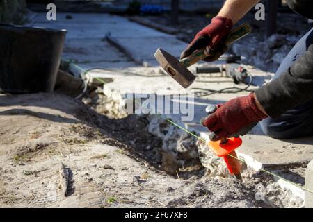 Defocus construction worker. Male hands in red work gloves hold a hammer and chisel. The paver paver works under the line. The atmosphere of the const Stock Photo