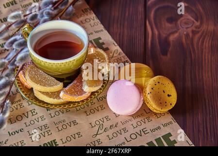 A ceramic green cup of tea, various sweets and willow branches on a paper napkin with the inscription love. Stock Photo