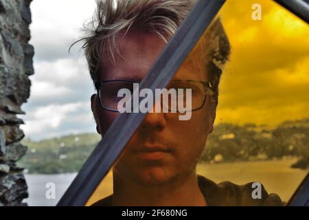 Young Man in Glasses Looking Through a Pane of Yellow Glass Stock Photo