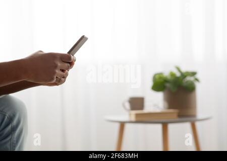 Gadget addiction concept. Unrecognizable black man holding mobile phone and surfing web, side view with copy space Stock Photo