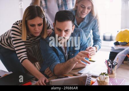 Group of curious smiling coworkers standing around their boss and watching project on a tablet. Stock Photo