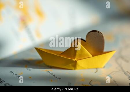 isolated origami yellow boat with wooden heart on world map. travel, sail or cruise concept, shipping or transportation through the sea. Stock Photo