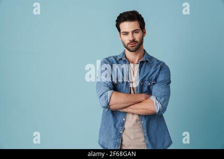 Young handsome man standing with hands crossed at camera isolated over blue background Stock Photo