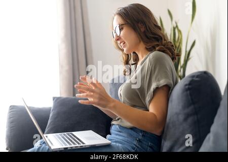 Side view of confident female employee holding video conference on the laptop, smart young woman using computer app for video communication with colleagues, video call on the distance Stock Photo