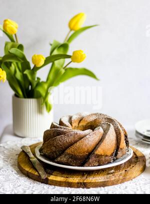 Easter table with freshly baked, vegan, traditional Polish Easter babka cake - layer of citrus and chocolate sponge, sprinled with powdered sugar. Stock Photo