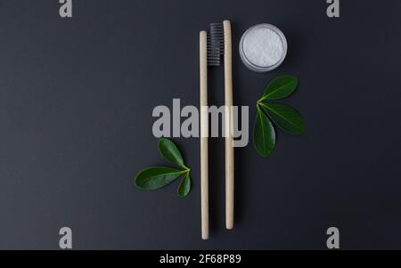 two wooden bamboo eco friendly toothbrushes, dentifrice and green leaves on black background.  Stock Photo