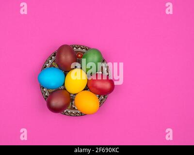 Bright colored eggs at Easter lie in a plate. Pink background. Stock Photo