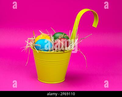Easter eggs on the hay in a bright bucket. Pink background. Stock Photo