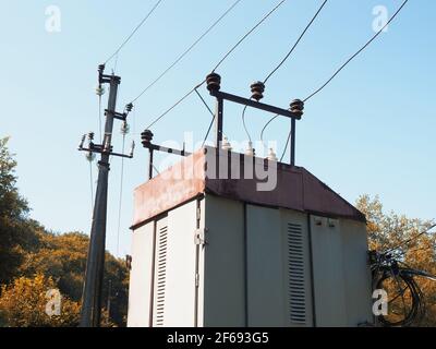 Top of a transformer booth with power lines against background of blue sky and trees Stock Photo