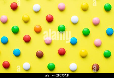 Colored balls of sugar on a yellow background. Chocolate candies covered with multicolored sugar glaze. Stock Photo