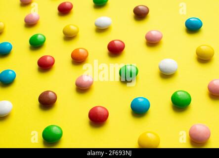 Colored balls of sugar on a yellow background. Chocolate candies covered with multicolored sugar glaze. Stock Photo