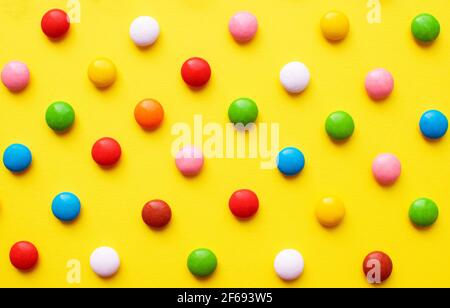 Colored balls of sugar on a yellow background. Chocolate candies covered with multicolored sugar glaze. Stock Photo