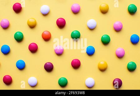Colored balls of sugar on a yellow background. Chocolate candies covered with multicolored sugar glaze. Stock Photo