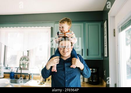 smiling father holding his son on his shoulders in kitchen