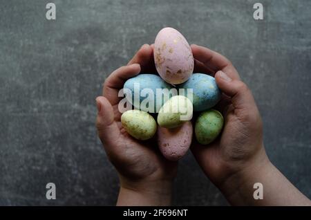 Easter colored eggs in hands on a gray background, hands in the center Stock Photo