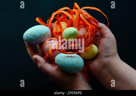 easter eggs with orange ribbon in hands on dark background, free space Stock Photo
