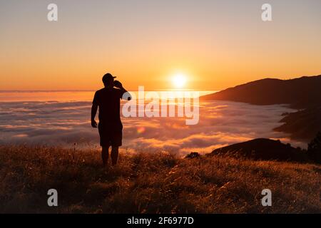 Hiking drinking a beer on top of mountain enjoying a sunset Stock Photo