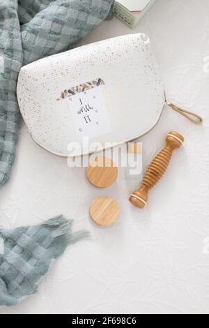 Closeup view of a toilet handbag with a positive message pasted on it next to a set of bamboo cosmetics for body care on a white comfortable quilt. Stock Photo