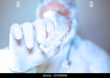A Doctor wearing surgical mask and surgical gloves holding a Covid-19 (corona virus) rapid test individually on white background with positive result. Stock Photo