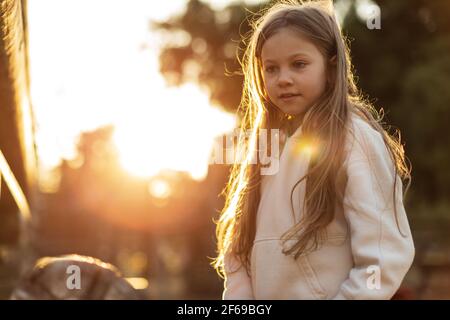 Little Caucasian blonde girl a in the park, in the rays of the setting sun. High quality photo
