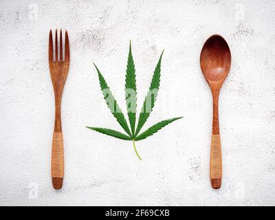 Food conceptual image of a cannabis leaf  with spoon and fork on white concrete background. Stock Photo