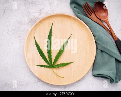 Food conceptual image of a cannabis leaf  with spoon and fork on white concrete background. Stock Photo