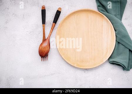 Empty wooden plate and green linen napkin with wooden spoon on white concrete  background . Stock Photo