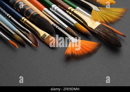 Artistic paintbrush for watercolor painting closeup. Different shape and size paint brushes on black paper background. Set of brushes for painting. Stock Photo