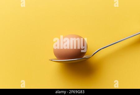 single brown chicken egg in a spoon on yellow background Stock Photo