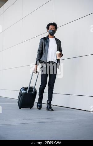 Tourist man carrying suitcase while walking outdoors. Stock Photo