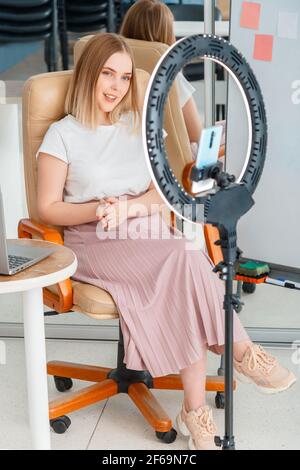 Online training presentation. Elearning webinar recording using circular lamp smartphone. Young woman teacher or blogger influencer near whiteboard in Stock Photo