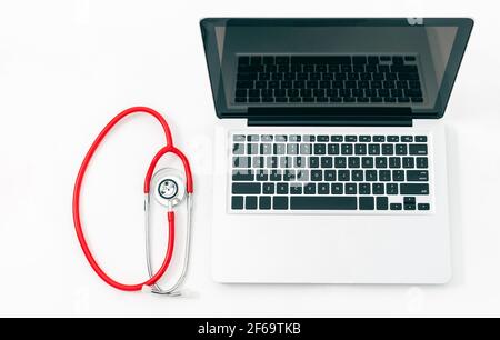 Rolled red stethoscope next to a laptop computer with open monitor isolated on a white background Stock Photo