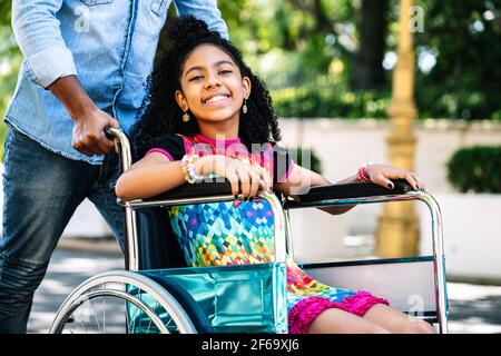 Little girl in a wheelchair enjoying a walk with her father. Stock Photo