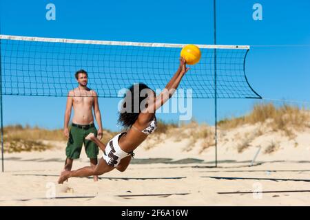 Group of friends – here two women and a man - playing beach volleyball, one in front having the ball Stock Photo