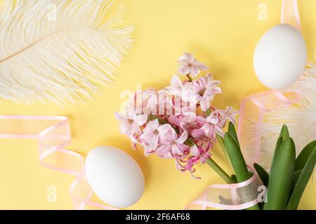 hyacinth flowers with two white eggs, and white feathers, and pink ribbon on pastel yellow colors. Happy Easter concept. Easter background. Top view Stock Photo