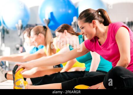 Group of four people in colorful cloths in a gym doing aerobics or warming up with gymnastics and stretching exercises Stock Photo