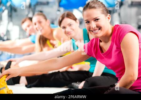 Group of four people in colorful cloths in a gym doing aerobics or warming up with gymnastics and stretching exercises Stock Photo