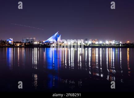 Panoramic view of the distinctively sail-shaped illuminated clubhouse of Dubai Creek Golf and Yacht Club from across the Dubai Creek park Stock Photo