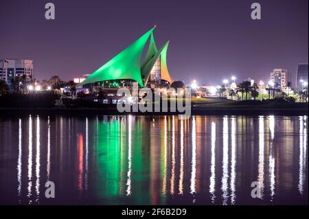 Panoramic view of the distinctively sail-shaped illuminated clubhouse of Dubai Creek Golf and Yacht Club from across the Dubai Creek park. Stock Photo
