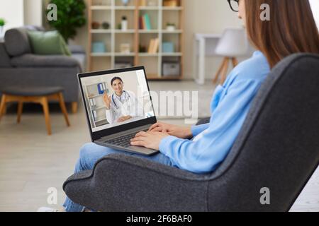 Woman sitting in chair with laptop and having video conference with online doctor Stock Photo