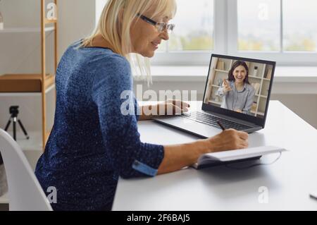 Mature lady taking notes while watching online lecture or having video call with coach Stock Photo